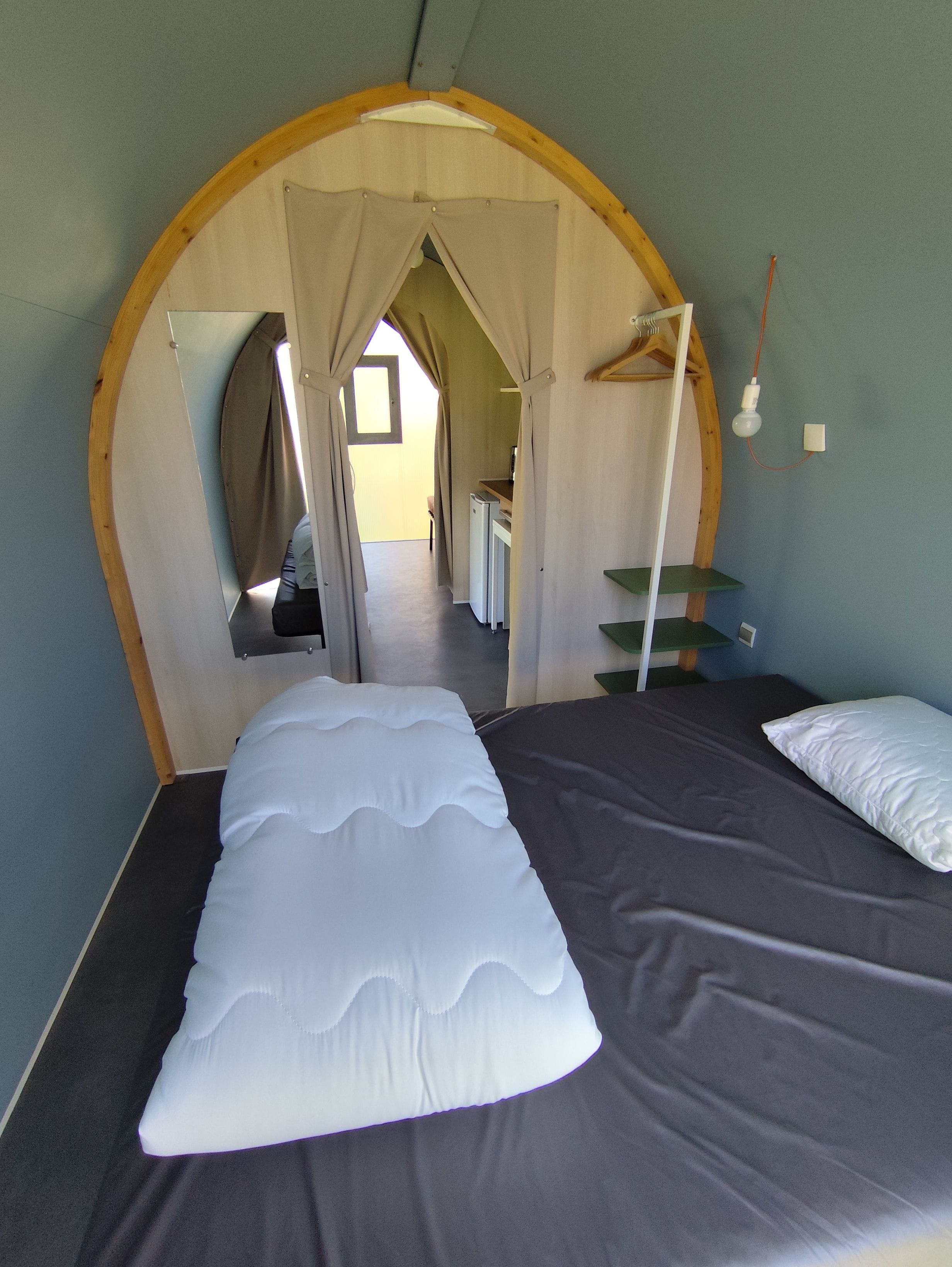 Une pièce avec un lit, un miroir, une lampe suspendue et une vue sur une autre pièce.
