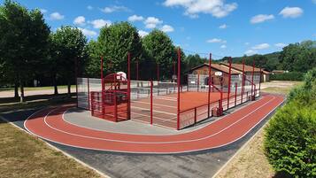 A running track with a red surface, surrounded by a red and white fence, and a basketball court with a red floor.