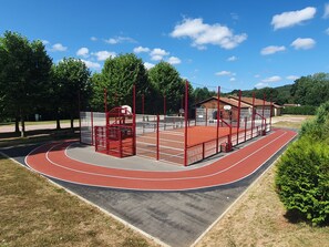 Pista de corrida com superfície vermelha, cercada por uma grade vermelha e branca, e quadra de basquete com piso vermelho.