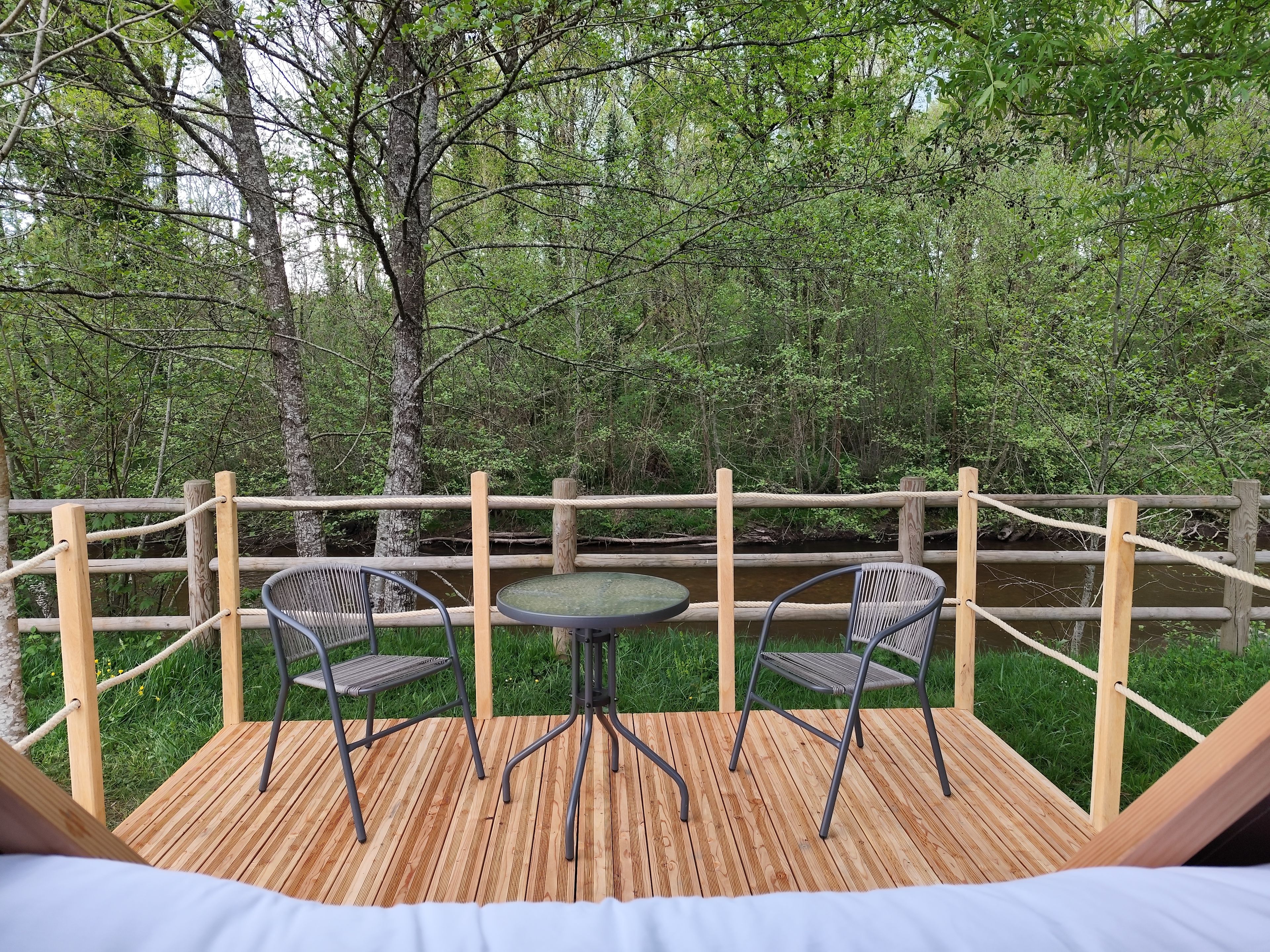 Une terrasse en bois avec deux chaises et une table, entourée d’une clôture en bois et d’une végétation luxuriante.