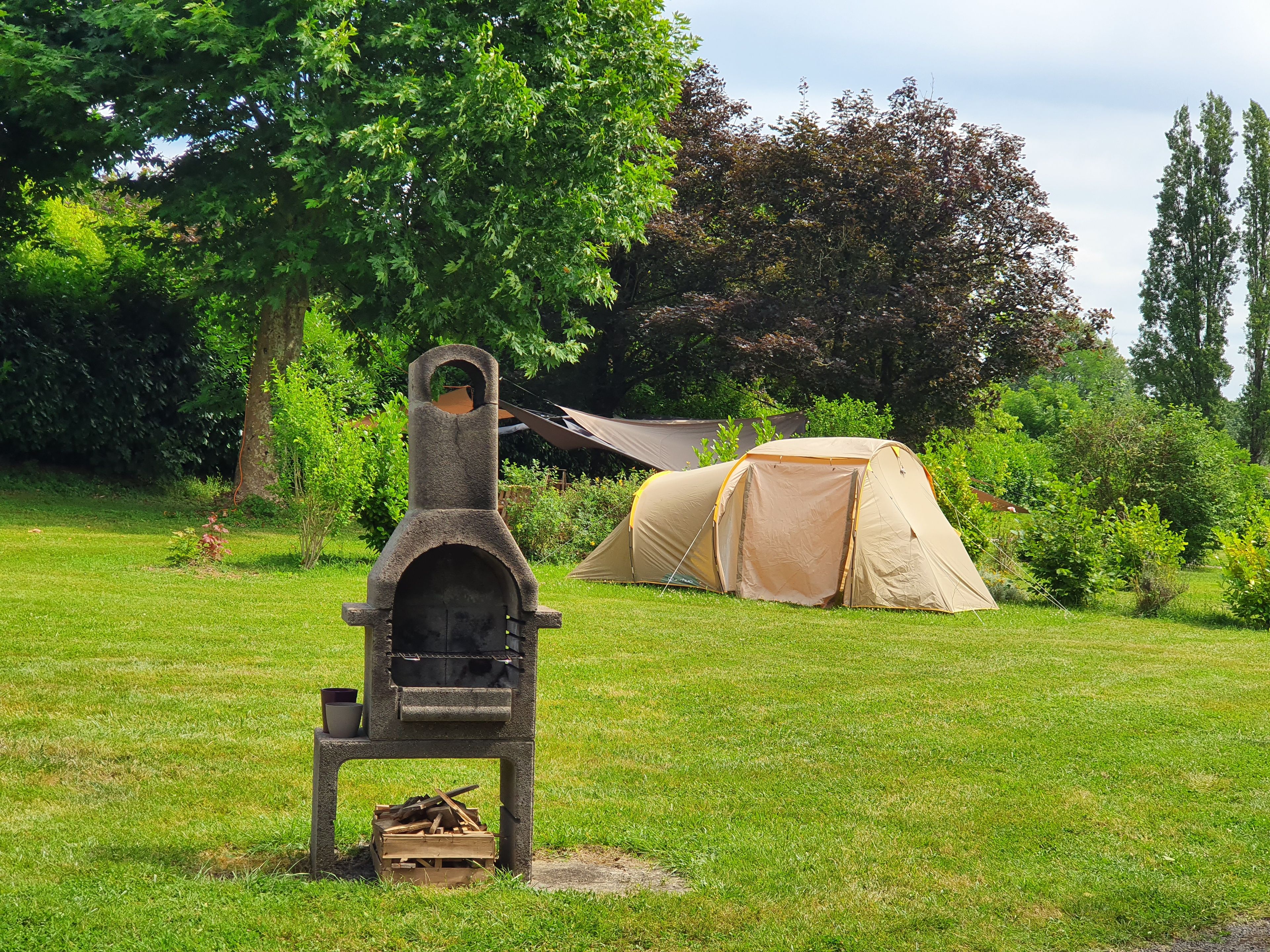 A camping area with a stone grill and a tent.