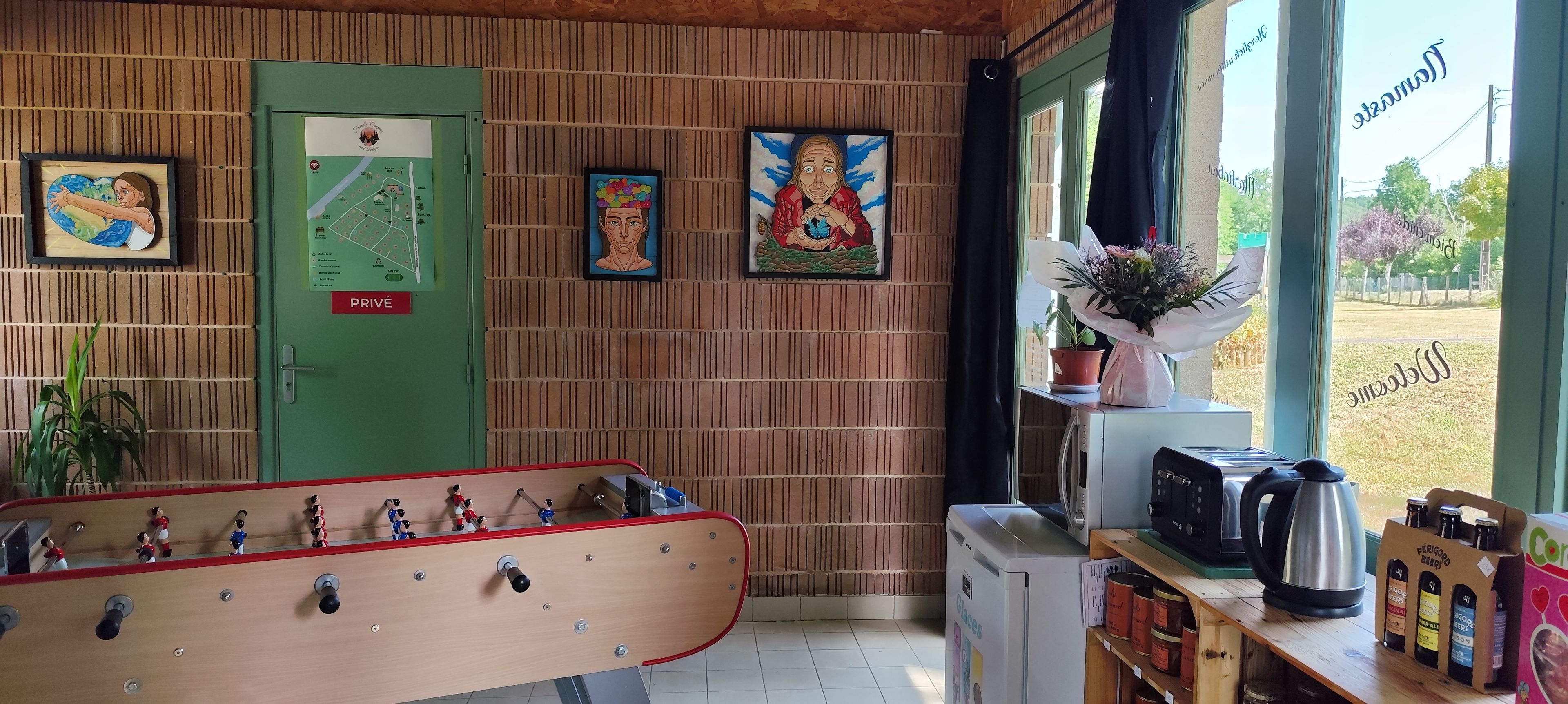 Une pièce avec un baby-foot, une porte verte portant l’inscription « PRIVÉ », et une fenêtre donnant sur l’extérieur.