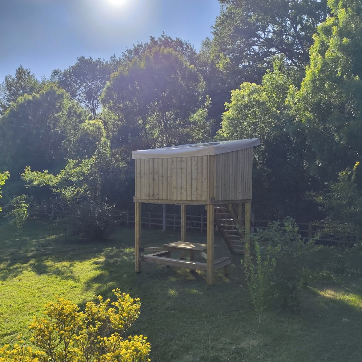 Une structure en bois dotée d’un toit plat, d’un escalier et d’une table de pique-nique.
