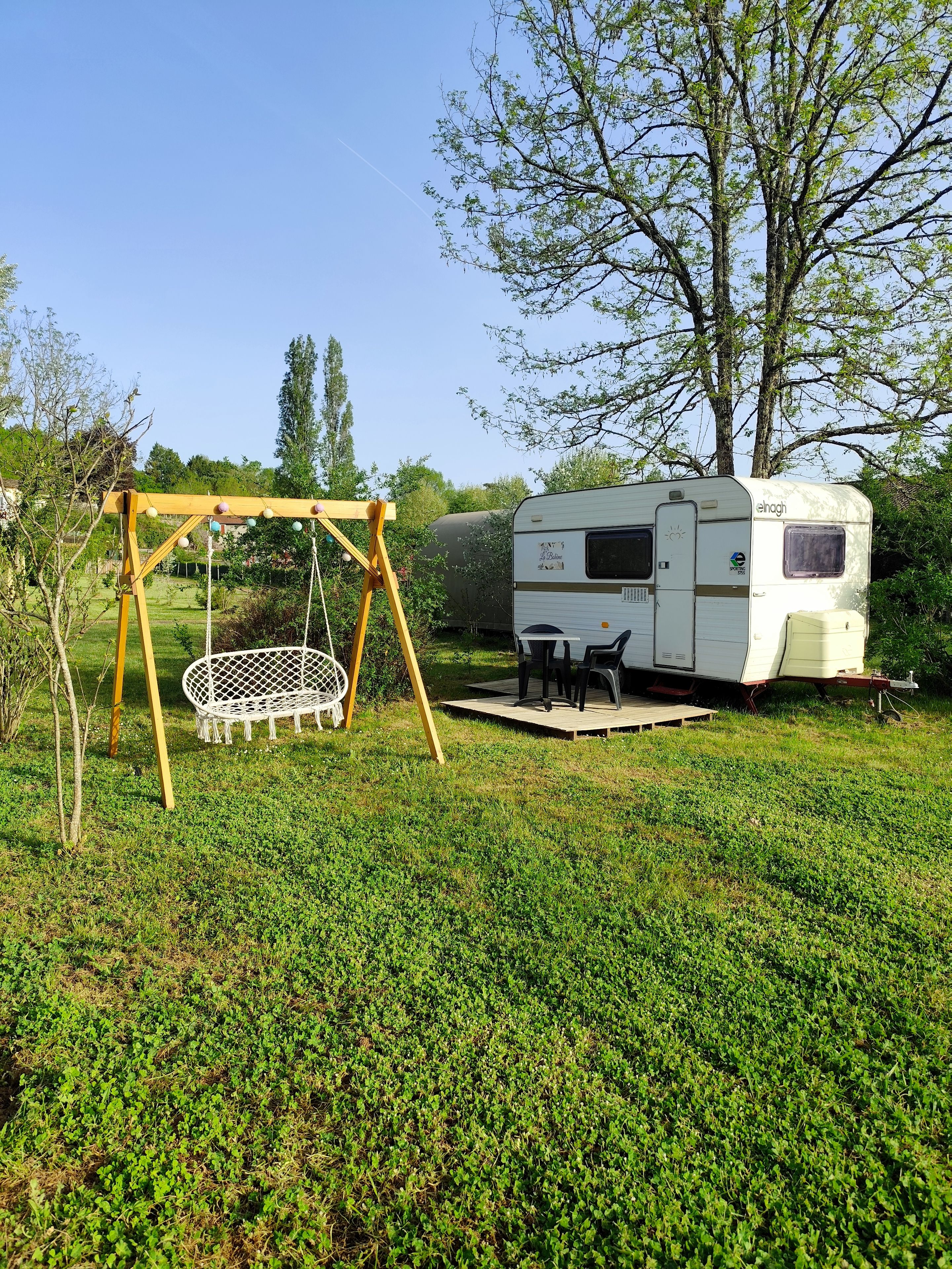 A recreational area with a swing set, a picnic table, and a white RV parked in a grassy field.