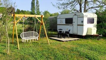 A recreational area with a swing set, a picnic table, and a white RV parked in a grassy field.