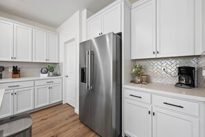 A modern kitchen with white cabinetry, a stainless steel refrigerator, and a coffee maker on the countertop. - Sleeps~12, 8-Beds 3-Baths, Backyard, Gameroom, Prime Location (Lincoln)
