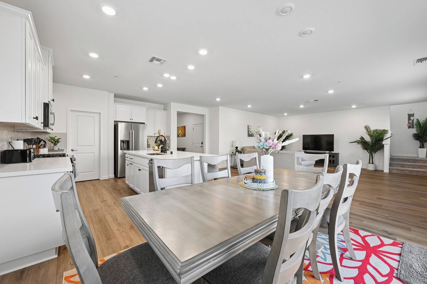 A modern kitchen with white cabinets, a stainless steel refrigerator, and a dining area with a wooden table and chairs.