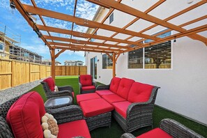 An outdoor patio with wicker furniture and red cushions, a pergola structure, and a view of a residential area. - Sleeps~12, 8-Beds 3-Baths, Backyard, Gameroom, Prime Location (Lincoln)