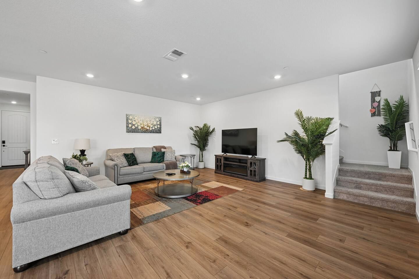 Un salon moderne avec un canapé gris, une table basse, un téléviseur à écran plat posé sur un meuble en bois et un escalier menant à un niveau supérieur.