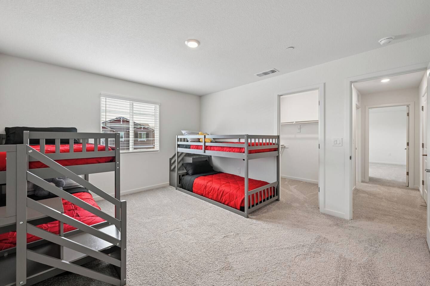 A room with bunk beds, a window with blinds, and a door leading to another room.