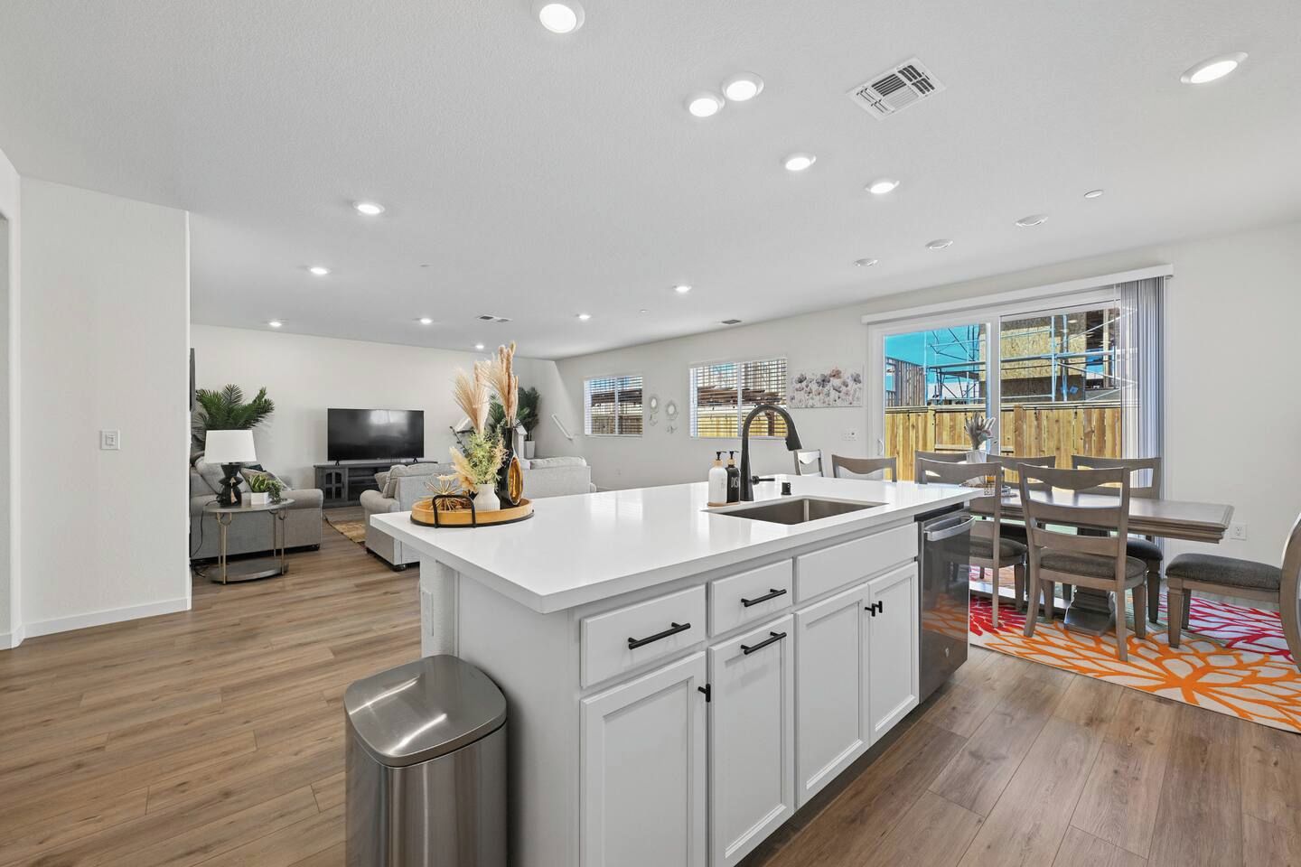 Cocina moderna con una isla central, armarios blancos y una zona de comedor con mesa y sillas.