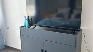 Ein grauer Schrank mit einem Flachbildfernseher darauf, einer Steckdose links und einem Kabel, das mit dem Fernseher verbunden ist.