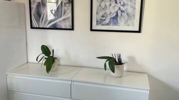 Ein weißer Schminktisch mit zwei Blumentöpfen, zwei gerahmten Blumenbildern an der Wand und einem dunklen Holzboden.