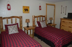 A room with two wooden beds, each with a red and black checkered bedspread and a compass pillow. There are two bedside tables with lamps, a wooden dresser, and wall decorations including a sign and arrows. - Marvelous 2-bedroom condo in Crested Butte for your getaway (Crested Butte)
