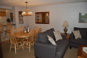 A dining area with a wooden table and chairs, a dark grey sofa with patterned cushions, a chandelier, and a mirror on the wall. - Marvelous 2-bedroom condo in Crested Butte for your getaway (Crested Butte)