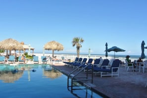 Un espace aménagé au bord de la piscine, avec des chaises longues et des parasols, un ciel dégagé et une vue sur l’océan.