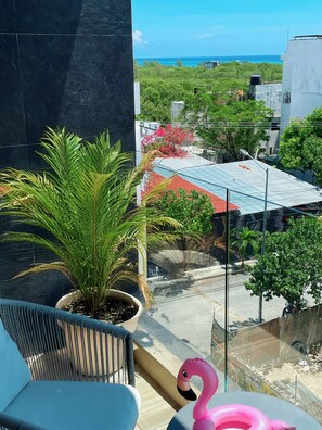 Un balcon agrémenté d’un pot de fleurs, d’une décoration représentant un flamant rose, et offrant une vue sur l’océan et les bâtiments.