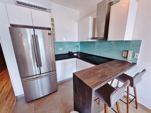 Une cuisine moderne avec un réfrigérateur en acier inoxydable, un comptoir-bar en bois et des armoires blanches.