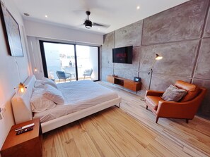 A modern bedroom with a large bed, a TV mounted on the wall, a seating area with a chair, and a balcony with a view. - On 5TH AVE! Studio OCEAN VIEW balcony & pool (Playa del Carmen)