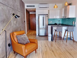 A modern kitchen with a stainless steel refrigerator, a bar area with stools, and a leather armchair. - On 5TH AVE! Studio OCEAN VIEW balcony & pool (Playa del Carmen)
