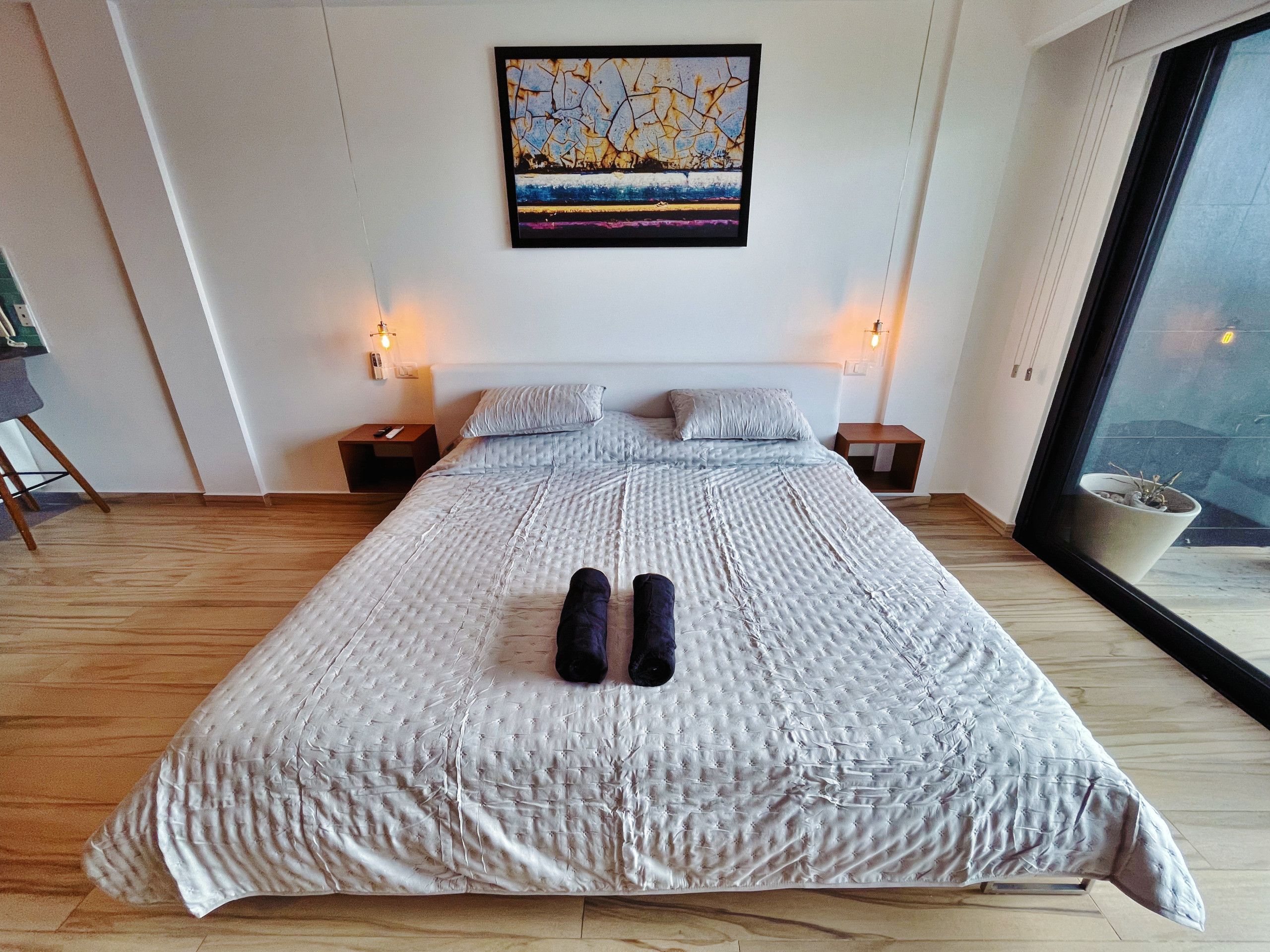A bedroom with a large bed, two bedside tables, a wall-mounted artwork, and a window with a view.