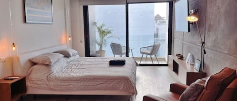 Un dormitorio moderno con cama, una silla, una planta en maceta y un balcón con vistas.