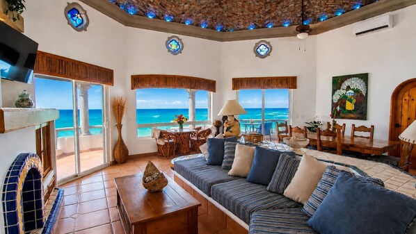 A spacious living room with a large sofa, dining table, and chairs, overlooking a scenic ocean view.