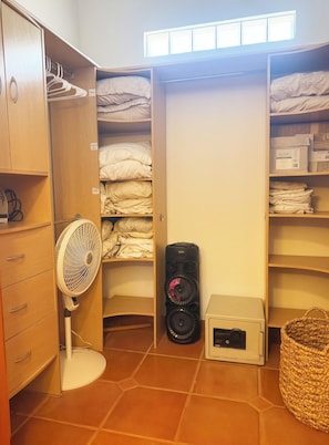 En lille opbevaringsplads med hylder til sammenfoldet tøj, en ventilator, en højttaler og en flettet kurv.