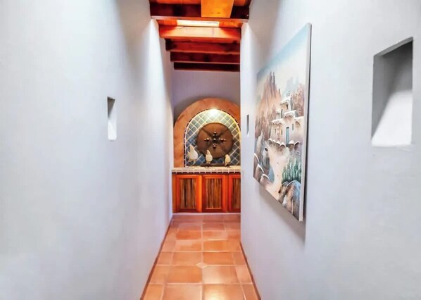 A hallway with a tiled floor, a wooden door with a decorative arch, and a wall-mounted painting.