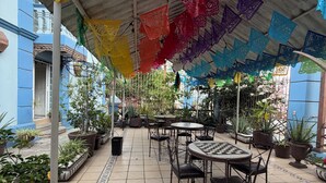 An outdoor patio area with tables and chairs, surrounded by potted plants and a colorful canopy. - Luz de Luna (Oaxaca)