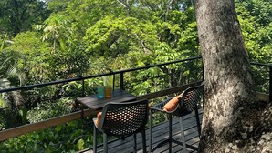 Una terraza al aire libre con una mesa y sillas, rodeada de exuberante follaje y árboles.