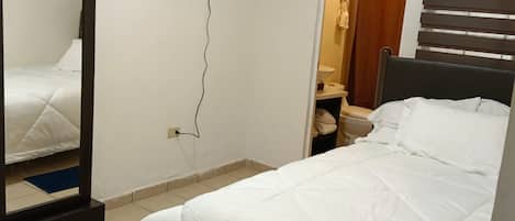 A bedroom with a bed, a mirror, an air conditioning unit, and a television on the wall.