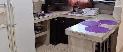 A kitchen with dark cabinets, a white refrigerator, a microwave, and a small island with purple mats.