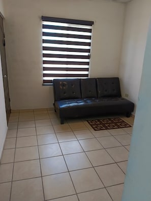 A room with a sofa, a window with blinds, and a tiled floor.