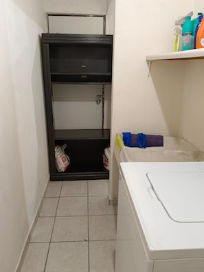 A laundry area with a washing machine, a metal shelf unit, and cleaning supplies.