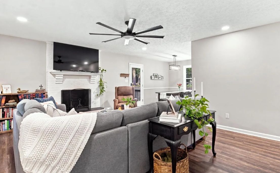A modern living room with a sectional sofa, a fireplace, a ceiling fan, and a bookshelf.