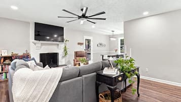 A modern living room with a sectional sofa, a fireplace, a ceiling fan, and a bookshelf.