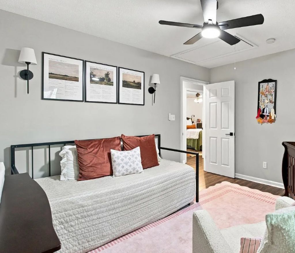 A bedroom with a bed, a ceiling fan, framed pictures on the wall, and a door leading to another room.
