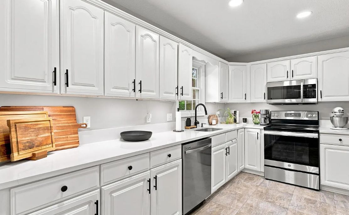 A modern kitchen with white cabinetry, stainless steel appliances, and a wooden cutting board.