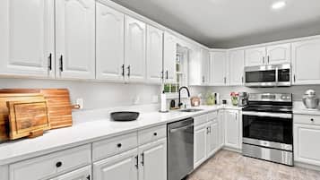 A modern kitchen with white cabinetry, stainless steel appliances, and a wooden cutting board.