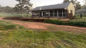 A single-story building with a large open porch area, surrounded by a fenced yard with a dirt path leading to the entrance.