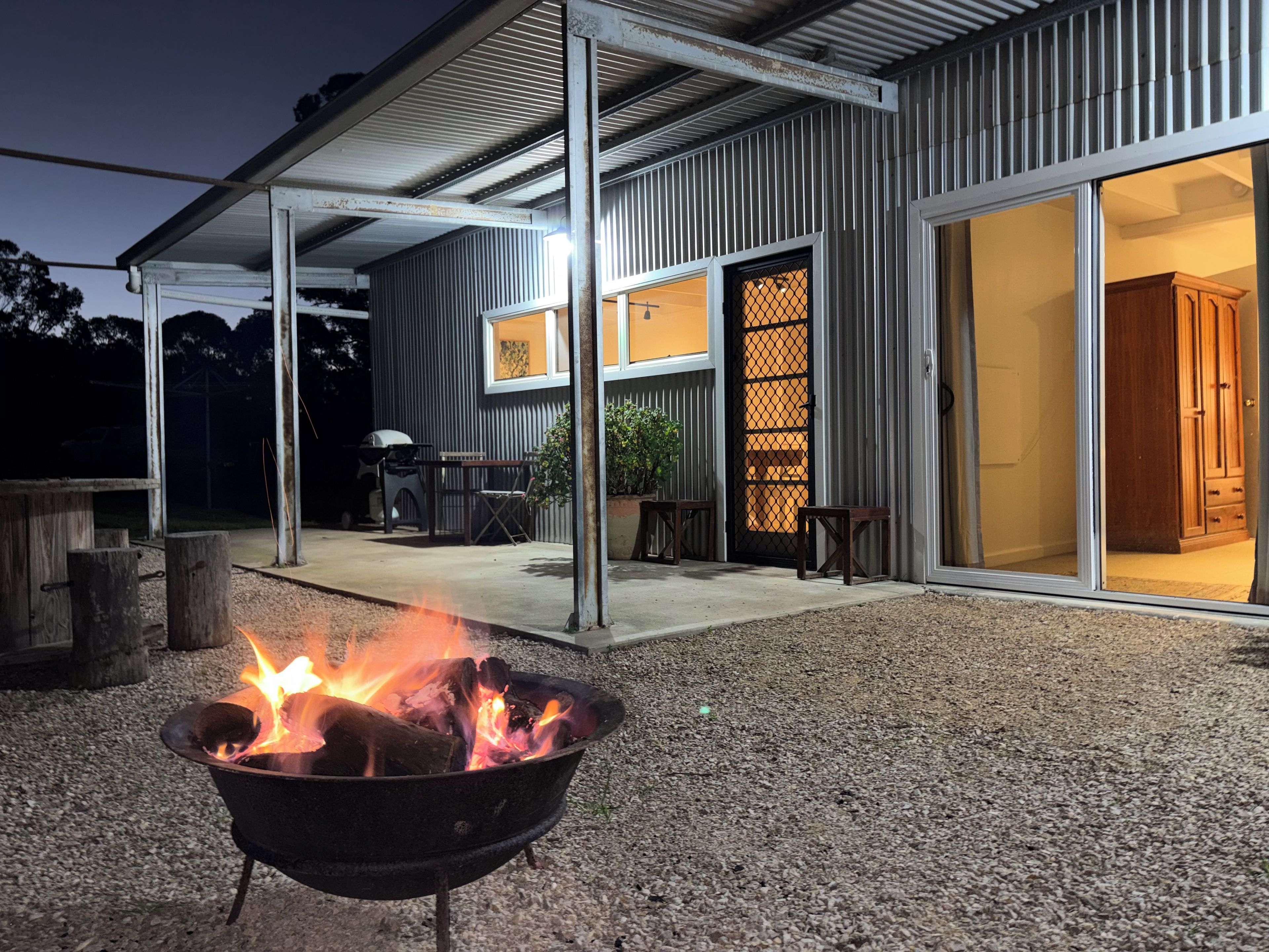 A covered outdoor area with a fire pit, a barbecue grill, and a dining table set up.