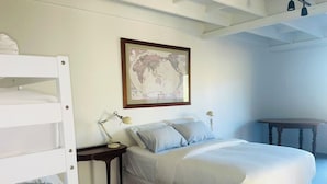 A bedroom with bunk beds, a single bed, a bedside table with lamps, and a world map on the wall.