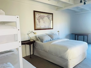 A bedroom with bunk beds, a single bed, a bedside table with lamps, and a world map on the wall.