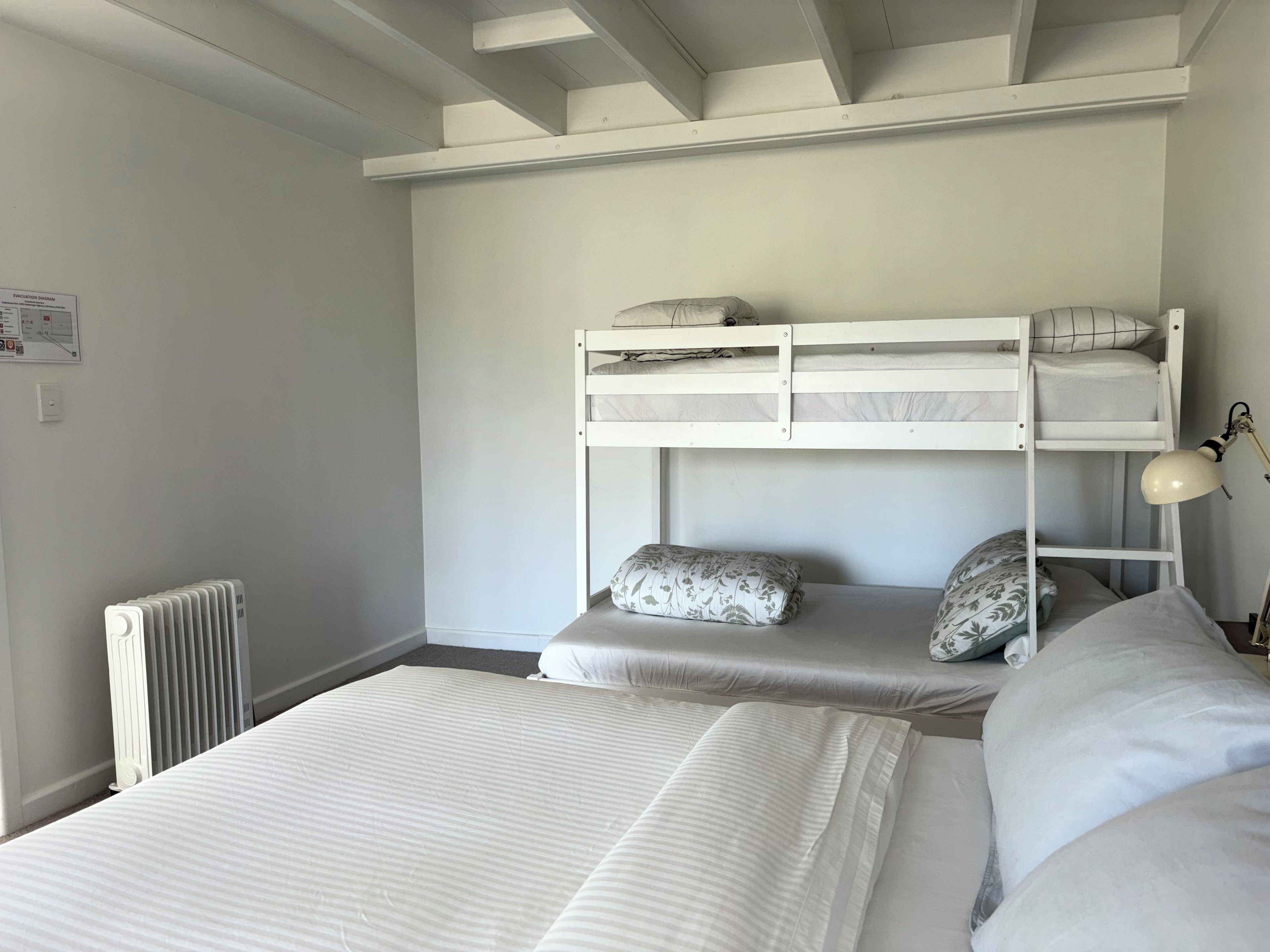 Une chambre avec un lit superposé, un radiateur, un bureau avec une lampe et un panneau de signalisation indiquant la sortie de secours, fixé au mur.