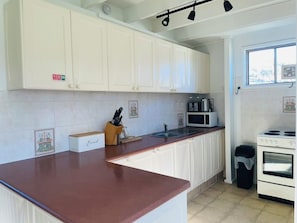A kitchen with white cabinets, a brown countertop, a sink, a microwave, a stove, and a trash bin.