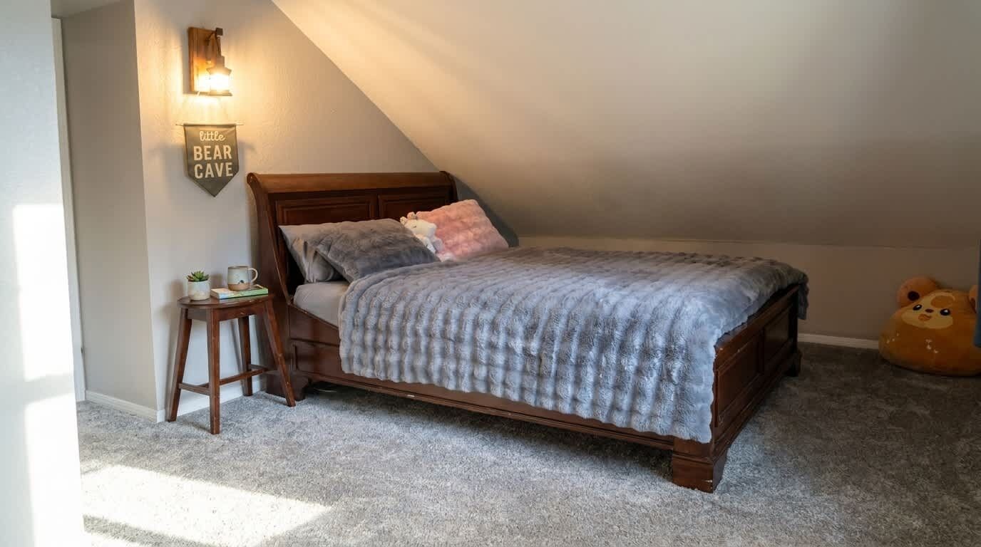 A bedroom with a sloped ceiling, a wooden bed, a nightstand, a lamp, and a teddy bear on the floor.