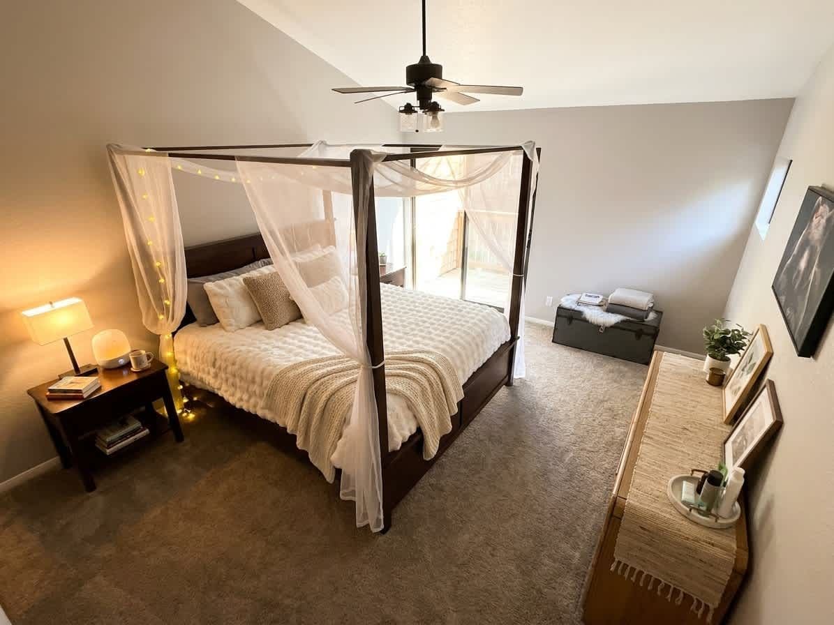 Un dormitorio con cama con dosel, mesita de noche, lámpara y ventilador de techo.