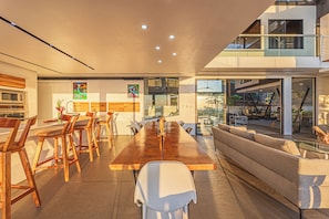 Cozinha moderna com uma longa mesa de madeira e cadeiras, um sofá e área de jantar com vista para o exterior.