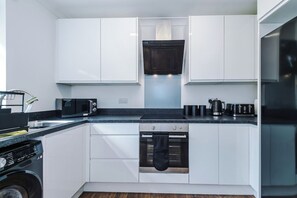 A compact kitchen with white cabinets, a built-in oven, a microwave, and a coffee machine. - Stylish 3-Bed Home in Leigh | Garden & Parking (Greater Manchester)